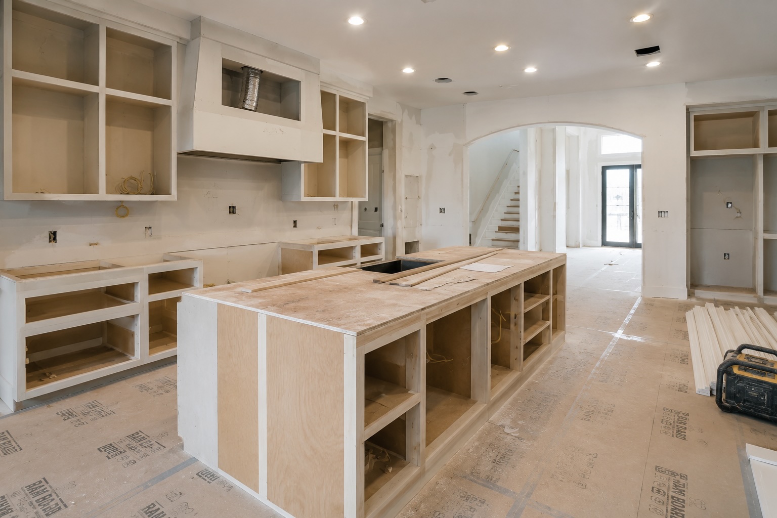 Greater Houston whole-home renovation jobsite mid-build with bare cabinet boxes installed, RAM BOARD floor protection, framed staircase, and finished arched entry